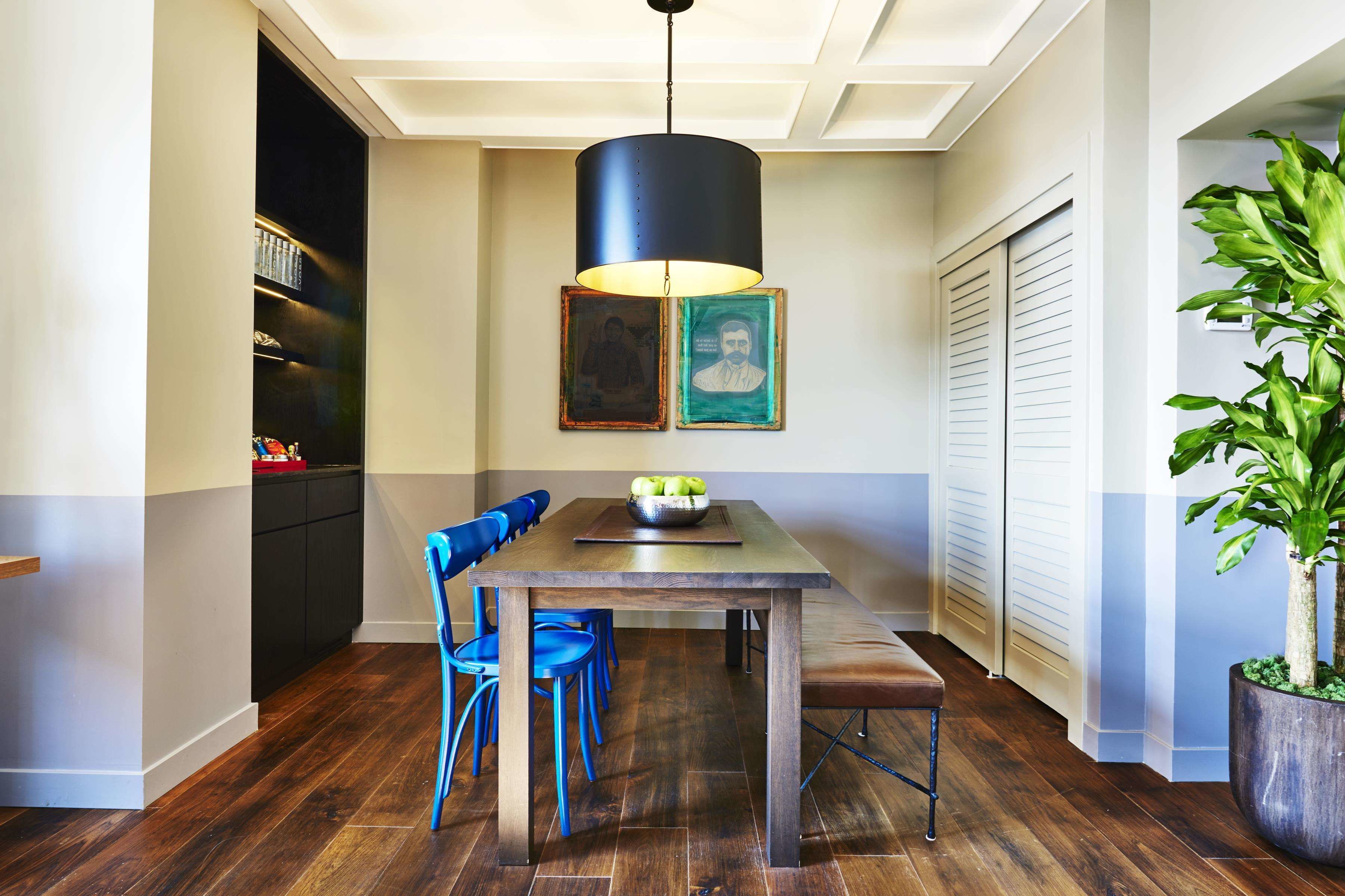 Un coin repas avec une table en bois, des chaises bleues, une suspension noire et une plante en pot.