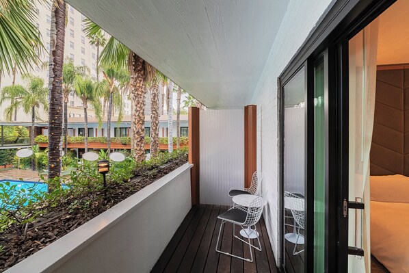 A balcony with a pool, white chairs, and a glass door leading to a room.
