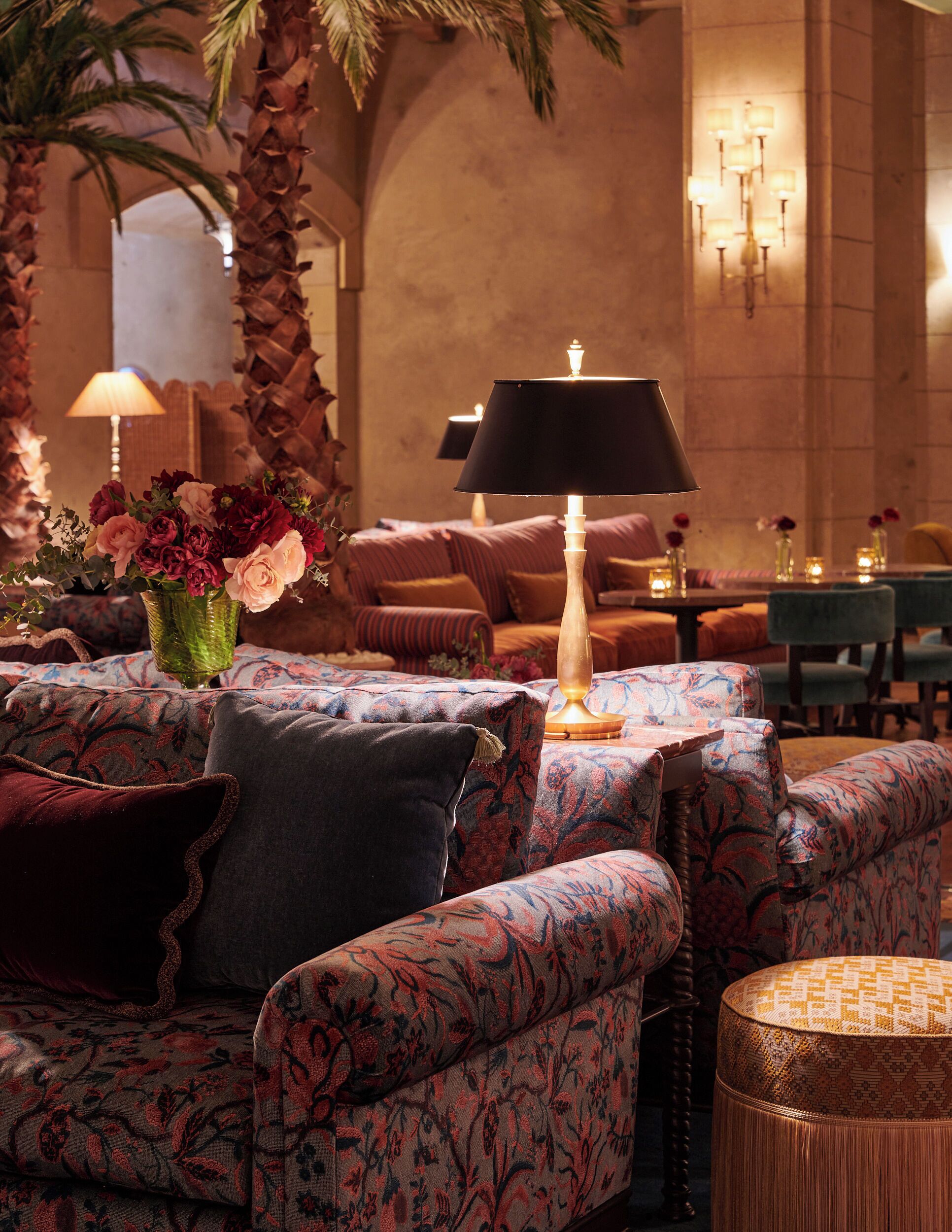 A cozy lounge area with patterned sofas, a central table with a lamp, and a vase of flowers.