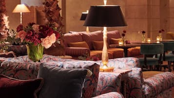 A cozy lounge area with patterned sofas, a central table with a lamp, and a vase of flowers.