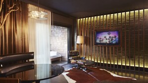 A modern living room with a leather sofa, a glass coffee table, a cowhide rug, a television mounted on a brick wall, and a lamp.