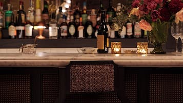 A bar area with a variety of bottles, a vase with flowers, and a candle on the counter.