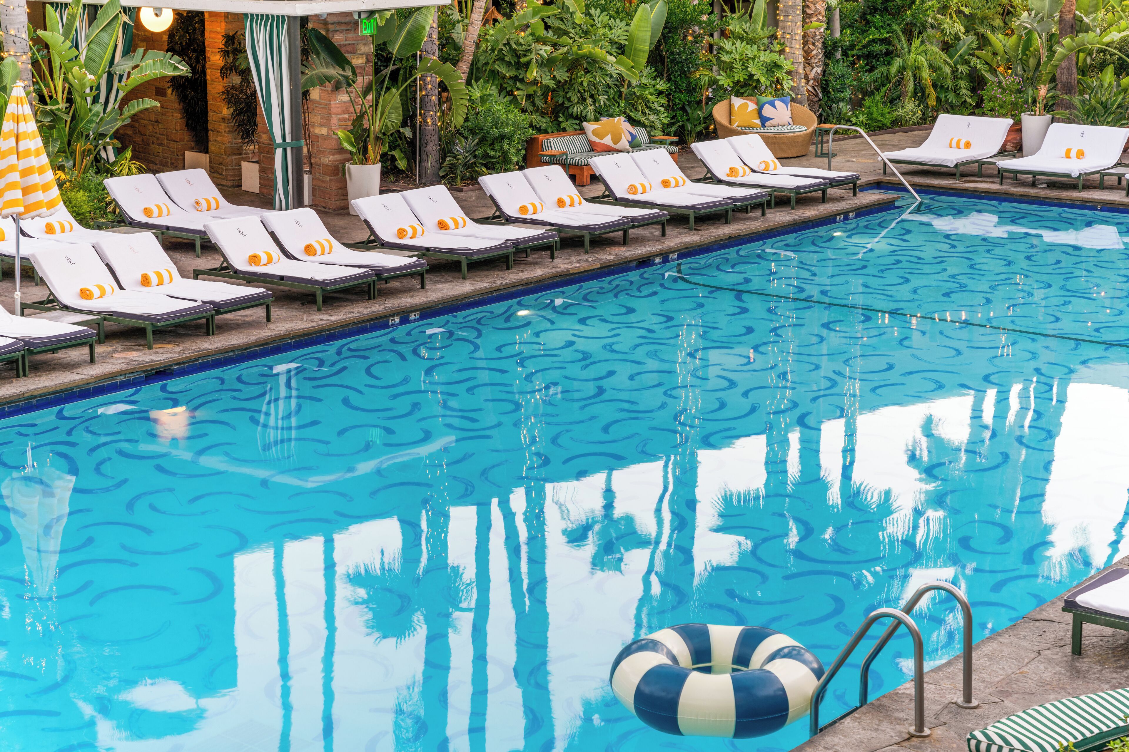 A pool with lounge chairs and umbrellas, surrounded by greenery.