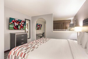Una habitación de hotel con una cama grande, un escritorio, una silla, un televisor montado en la pared y una ventana con cortinas.