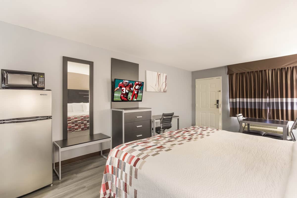 A hotel room with a bed, a desk, a chair, a television, a microwave, and a refrigerator.