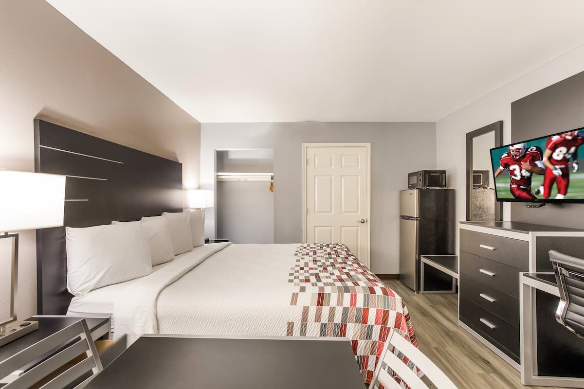 A modern hotel room with a bed, a desk, a TV, and a door.