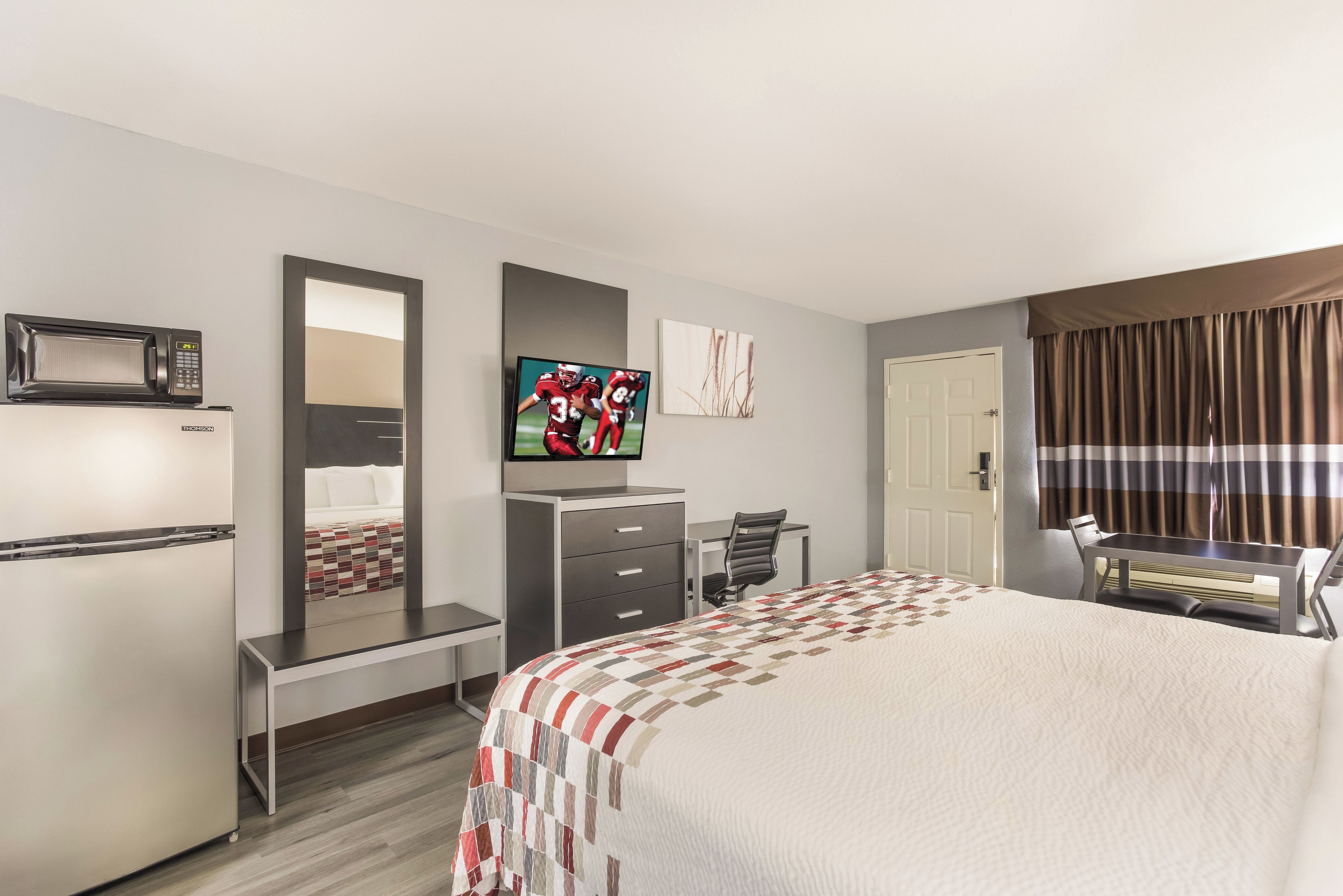 A hotel room with a bed, a desk, a chair, a television, a microwave, and a door.