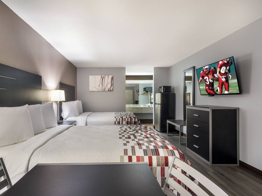 Quarto de hotel com duas camas, uma escrivaninha, televisão e cozinha compacta.