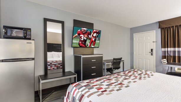A hotel room with a bed, a desk, a chair, a television, a microwave, and a door. - Red Roof Inn & Suites Athens, AL (Athens)