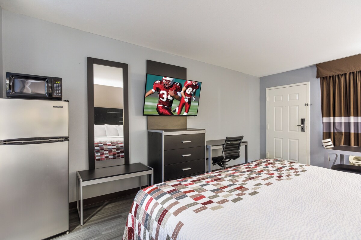 A hotel room with a bed, a desk, a chair, a microwave, a television, and a door.