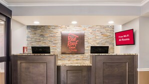 A reception area with a Red Roof Inn sign, a flat-screen TV displaying "Free Wi-Fi All Rooms," and a stone-patterned wall. - Red Roof Inn & Suites Athens, AL (Athens)