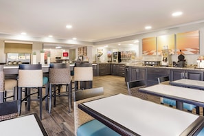 A modern restaurant with high tables and bar stools, a kitchen area, and a counter with various food items and a waffle maker. - Red Roof Inn & Suites Athens, AL (Athens)