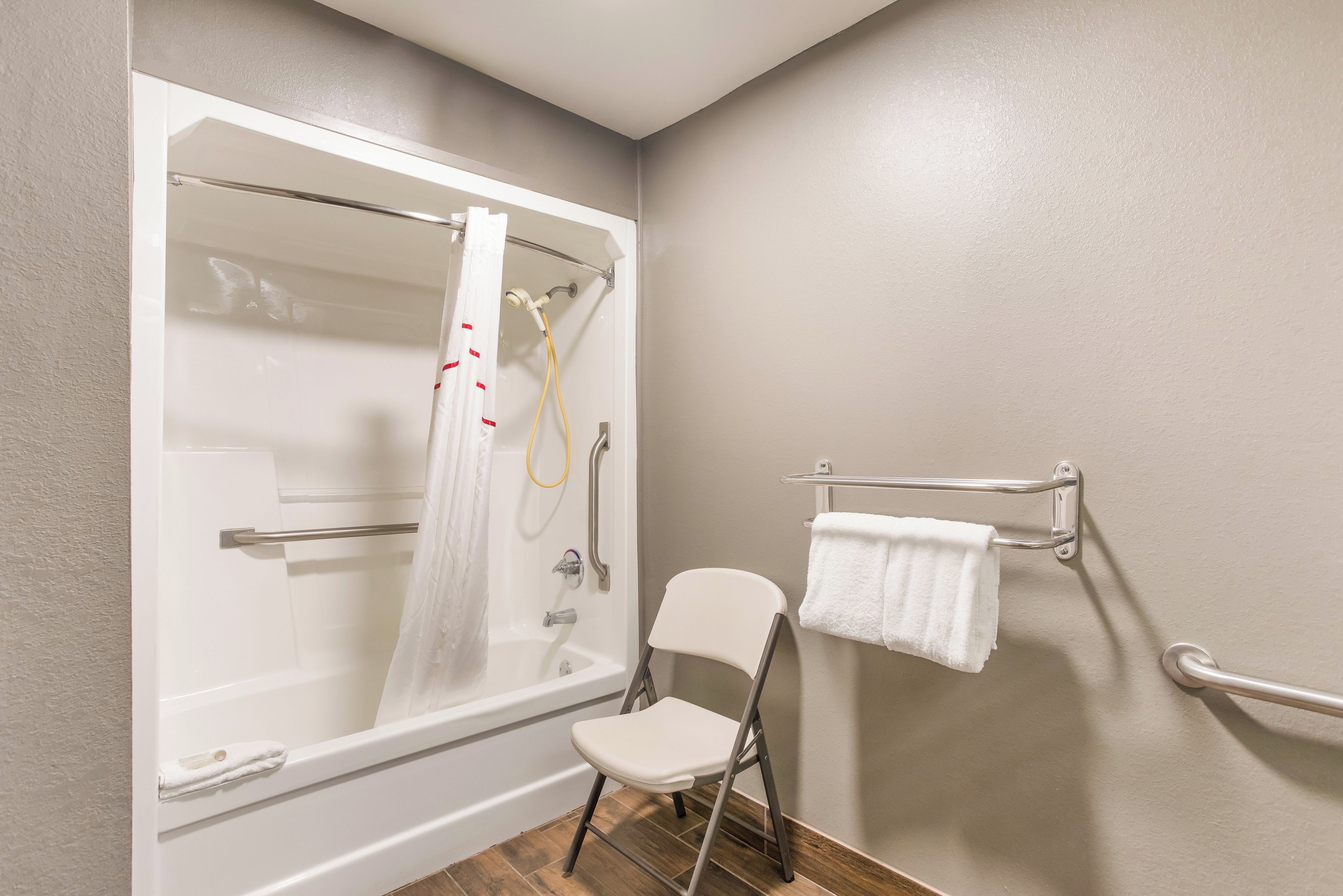 A bathroom with a bathtub, a shower, a white chair, and a towel rack.