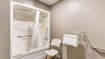 A bathroom with a bathtub, a shower, a white chair, and a towel rack.