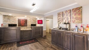 A hotel reception area with a stone wall, dark wooden reception desk, and a coffee station. - Red Roof Inn & Suites Athens, AL (Athens)