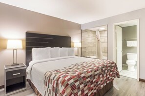 A hotel room with a bed, nightstand, and a bathroom visible through an open door. - Red Roof Inn & Suites Athens, AL (Athens)