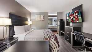 A modern hotel room with a bed, desk, chair, TV, and a kitchenette. - Red Roof Inn & Suites Athens, AL (Athens)