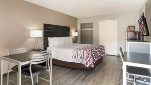 A hotel room with a bed, a desk, a chair, a TV, and a door.