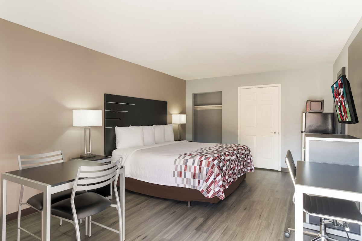 A hotel room with a bed, bedside table, lamp, desk, chair, and a TV.