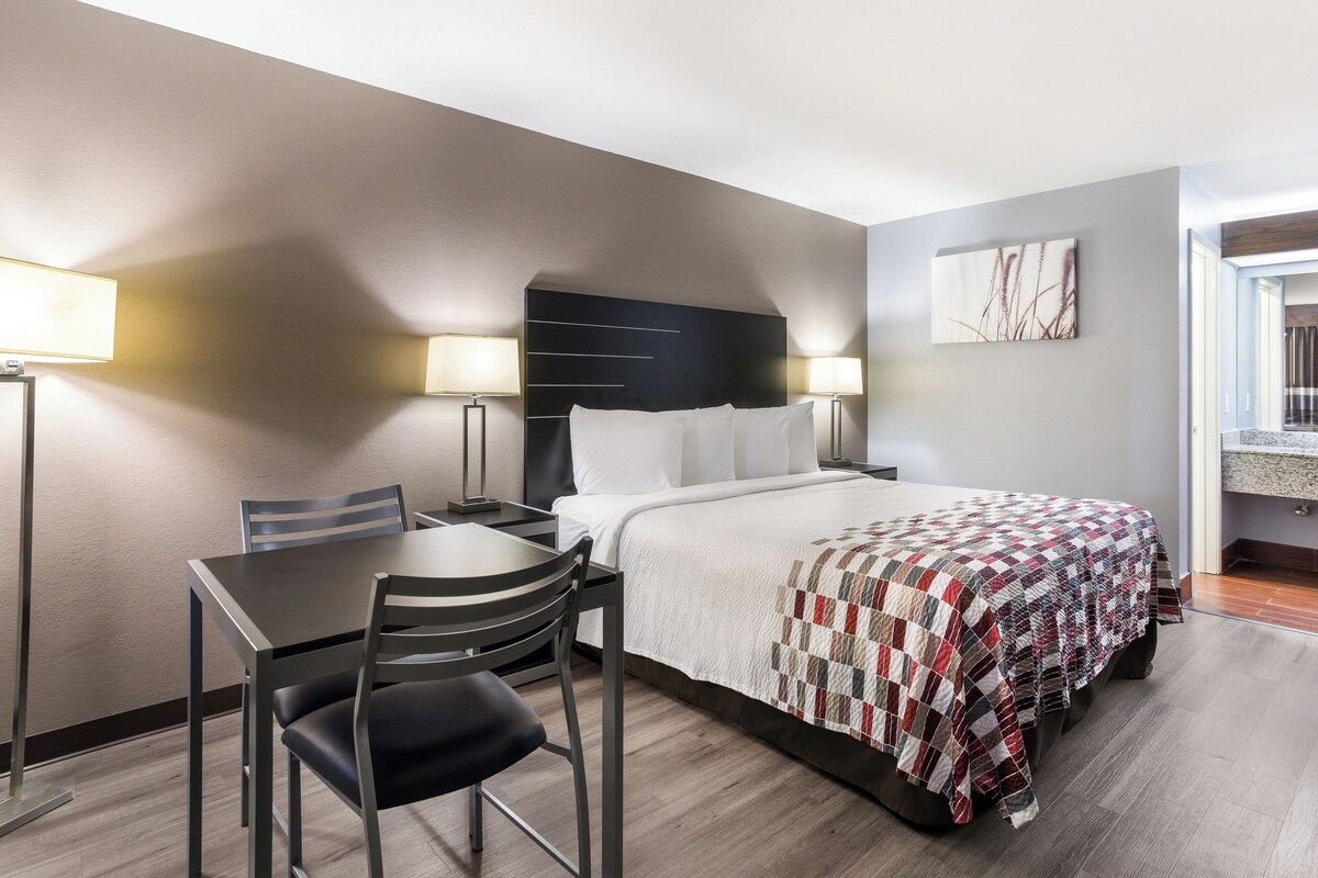 A hotel room with a bed, a desk, two chairs, and two bedside lamps.
