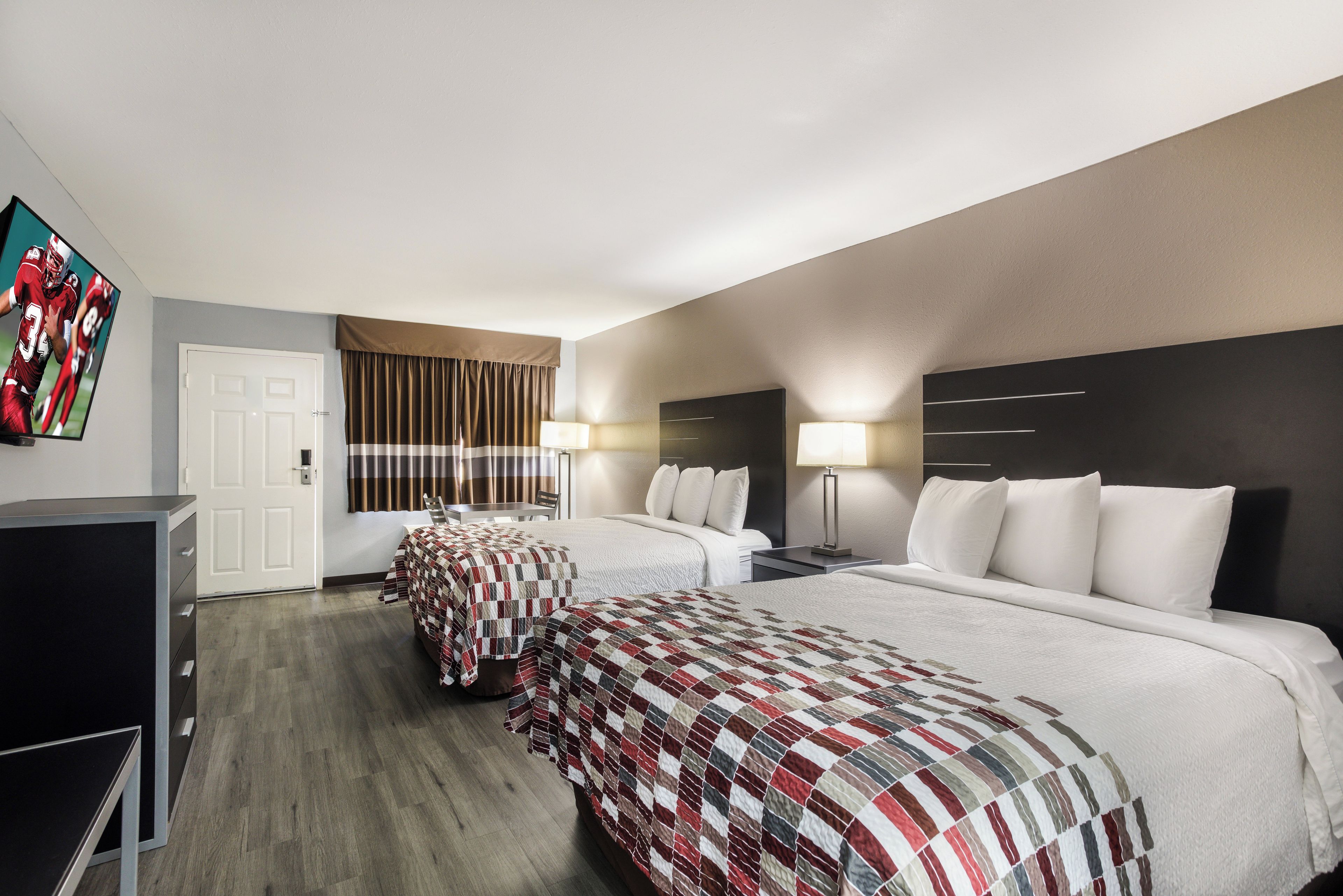 Quarto de hotel com duas camas, televisão, escrivaninha e uma cadeira.