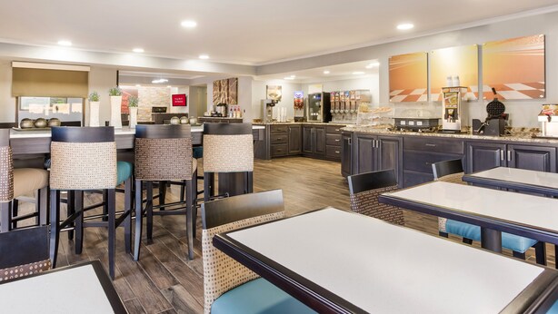 A modern restaurant with high tables and bar stools, a kitchen area, and a counter with various food items and a waffle maker. - Red Roof Inn & Suites Athens, AL (Athens)