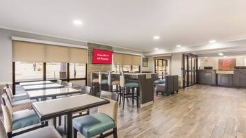 A restaurant with multiple tables and chairs, a red sign indicating free Wi-Fi, and a stone wall.