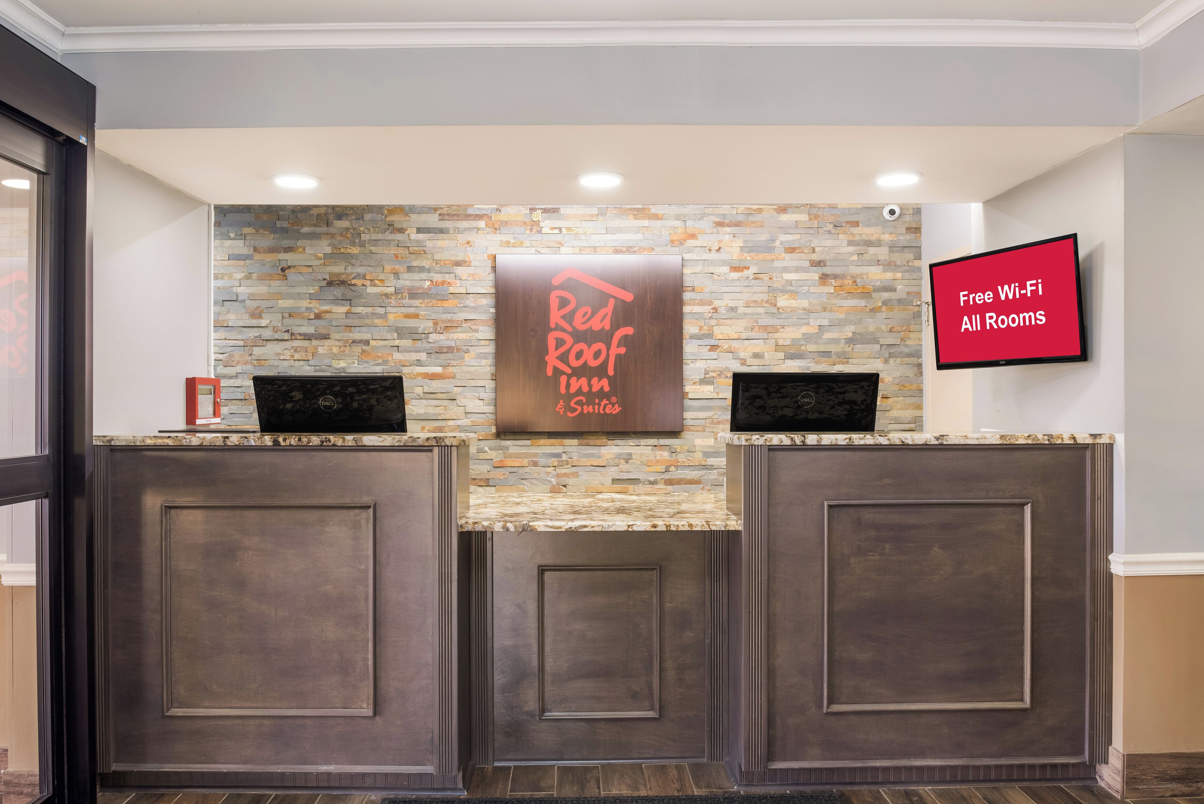 Un comptoir d’accueil avec un mur en pierre en arrière-plan, une enseigne Red Roof Inn et un écran numérique indiquant : « Wi-Fi gratuit dans toutes les chambres ».