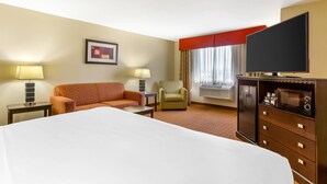 A hotel room with a large bed, a sofa, a chair, a TV, a dresser, and a window with curtains. - Comfort Inn Phoenix Central City (Phoenix)