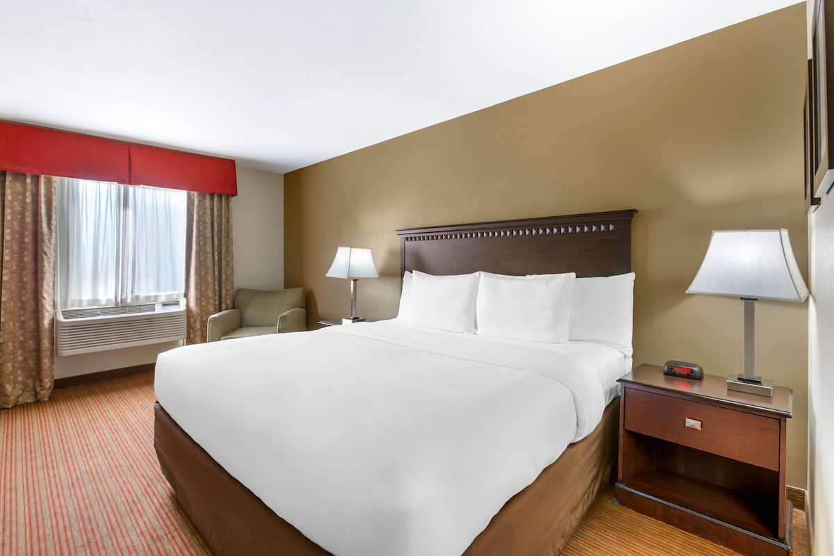 A hotel room with a large bed, two bedside tables with lamps, a chair, and a window with curtains.
