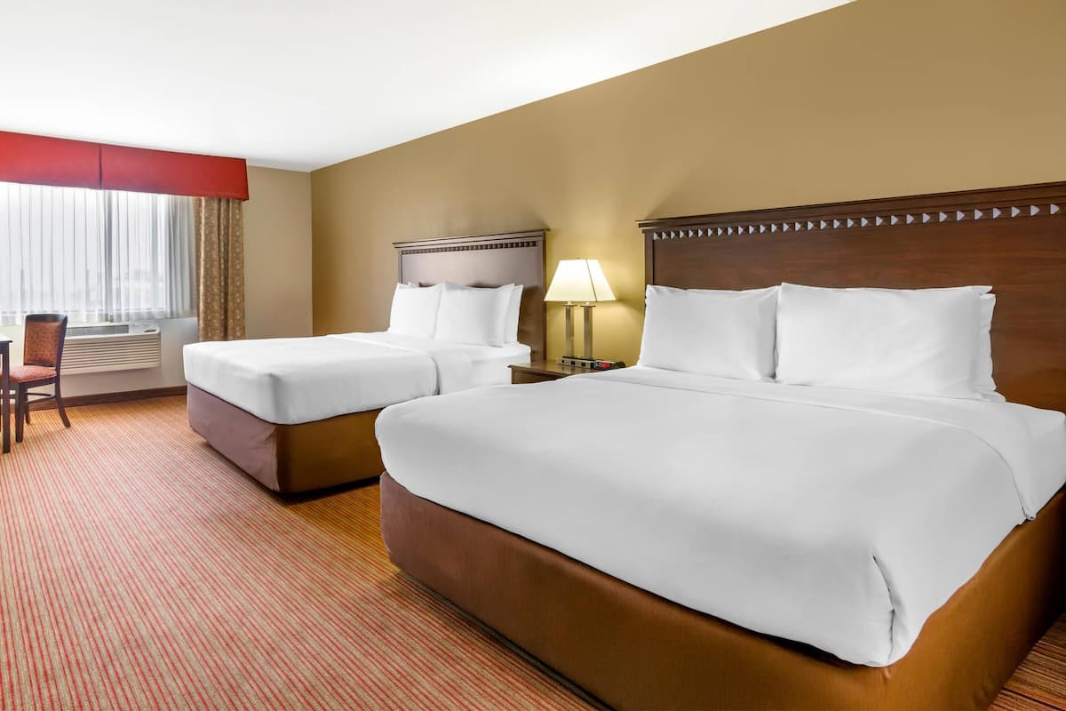 A hotel room with two beds, a desk, a chair, and a window with curtains.