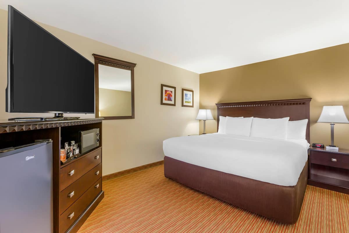 A hotel room with a large bed, a flat-screen TV, a minibar, and a desk with a lamp.