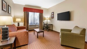 A hotel room with a sofa, a chair, a small table, a desk, a TV, and a window with curtains. - Comfort Inn Phoenix Central City (Phoenix)