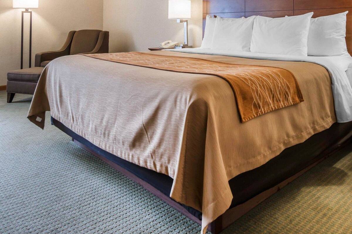 A hotel room with a large bed, two bedside lamps, a chair, and a nightstand with a phone.