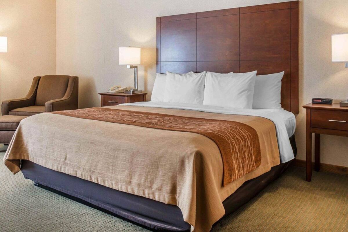 A hotel room with a large bed, two bedside tables, a chair, and a lamp.