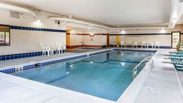 An indoor swimming pool with clear water, surrounded by white and green chairs, and a tiled floor.