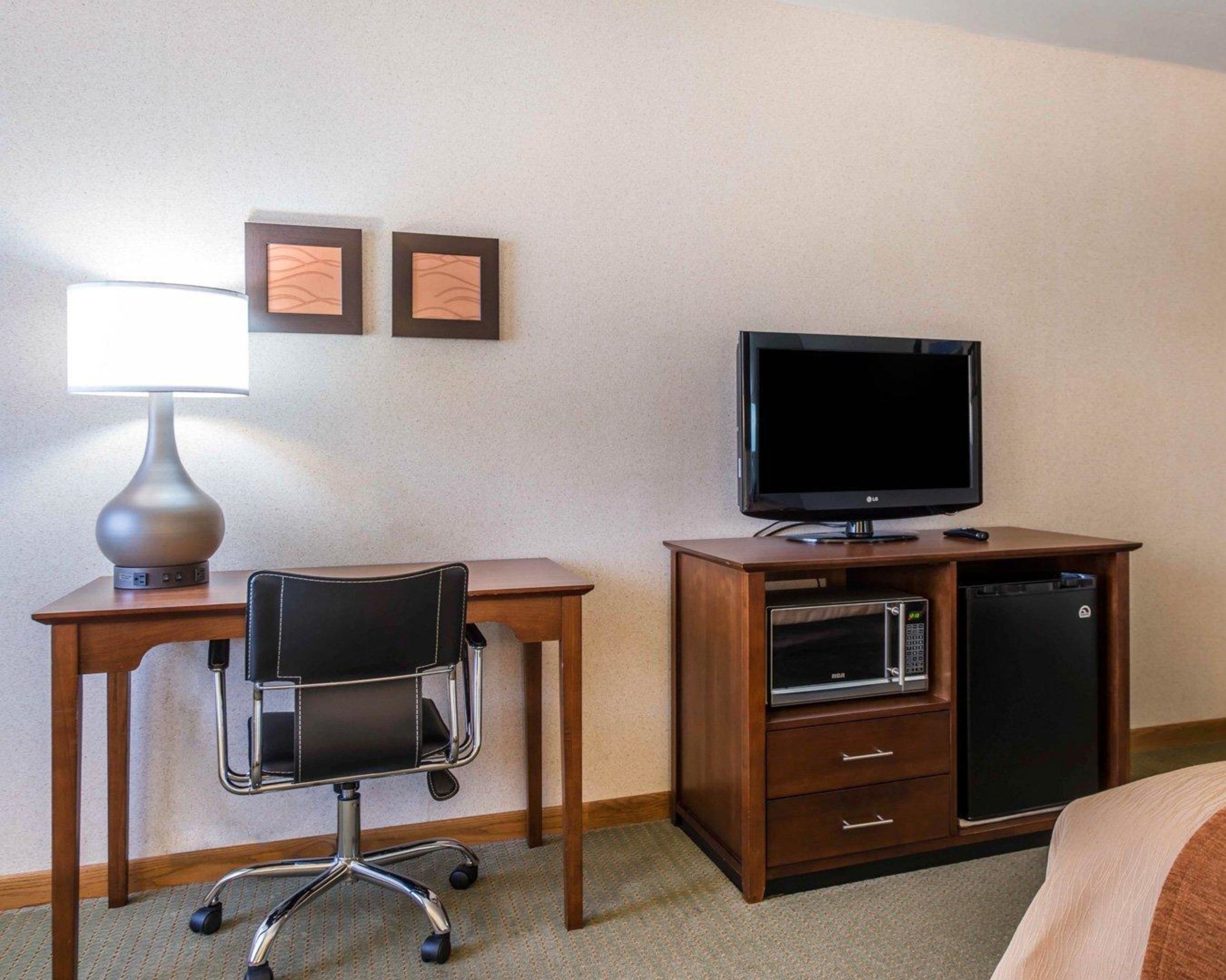 A hotel room with a desk, chair, lamp, television, and a minibar.