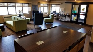 A hotel lobby with a wooden reception desk, green armchairs, a blue chair, and a small table with a lamp. There are informational posters on the wall and a window with blinds. - Comfort Inn Salida (Salida)
