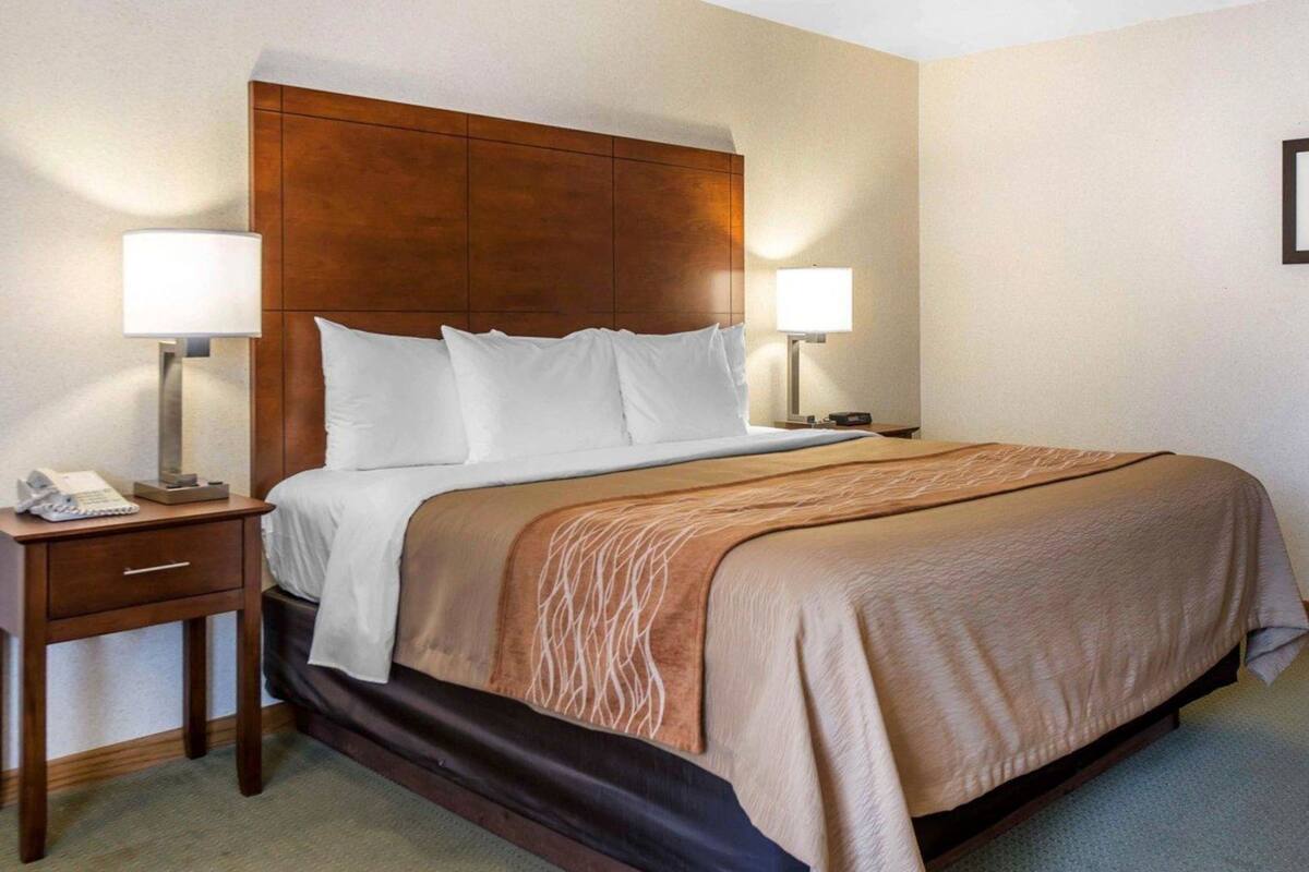 A hotel room with a wooden headboard, two bedside lamps, a telephone, and a bed with a brown blanket.
