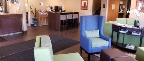 A hotel lobby with a reception desk, seating area with armchairs, a staircase, and a dining area.