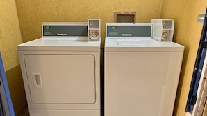 Two white wall-mounted washing machines with digital displays, a wooden door, and a concrete floor. - Welcome Inn (Milledgeville)