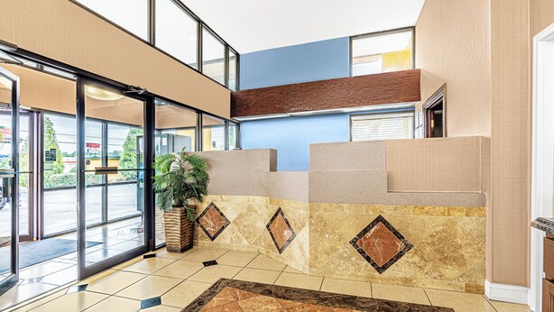 A lobby with a reception desk, a potted plant, and a patterned floor. - Welcome Inn (Milledgeville)