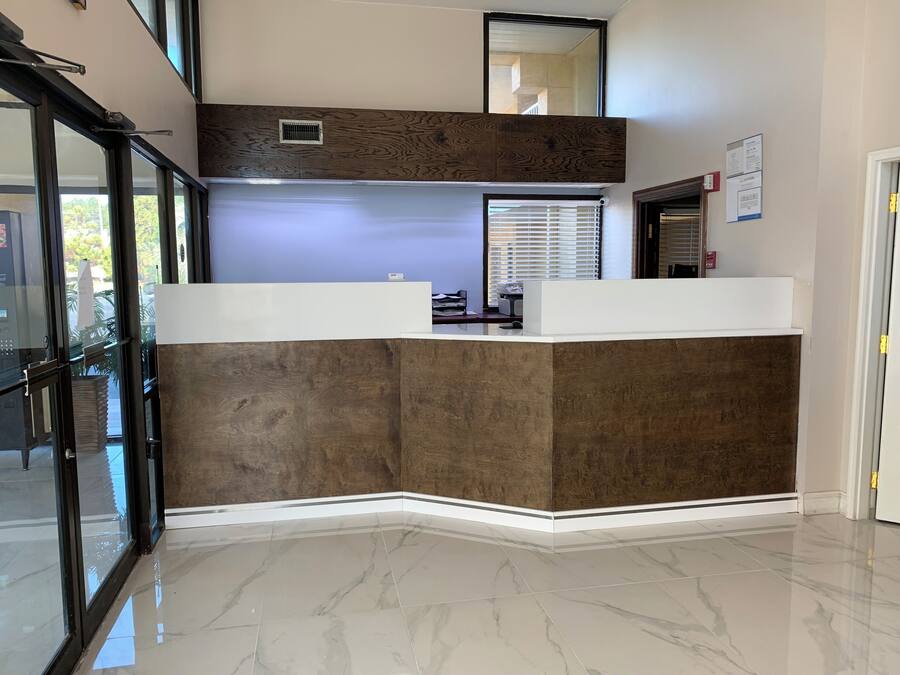 A reception desk with a modern design, a large window with blinds, and a clean, polished floor.
