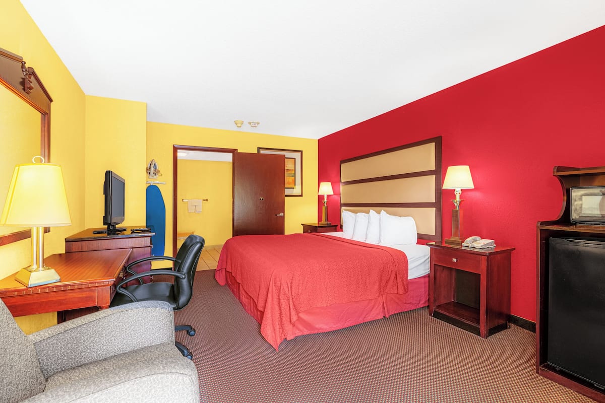 Quarto de hotel com cama, escrivaninha, cadeira, televisão e duas mesas de cabeceira com luminárias.