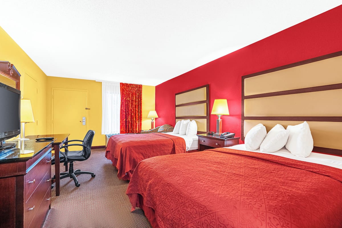 Quarto de hotel com duas camas, uma mesa de escritório com computador, uma cadeira e uma televisão.