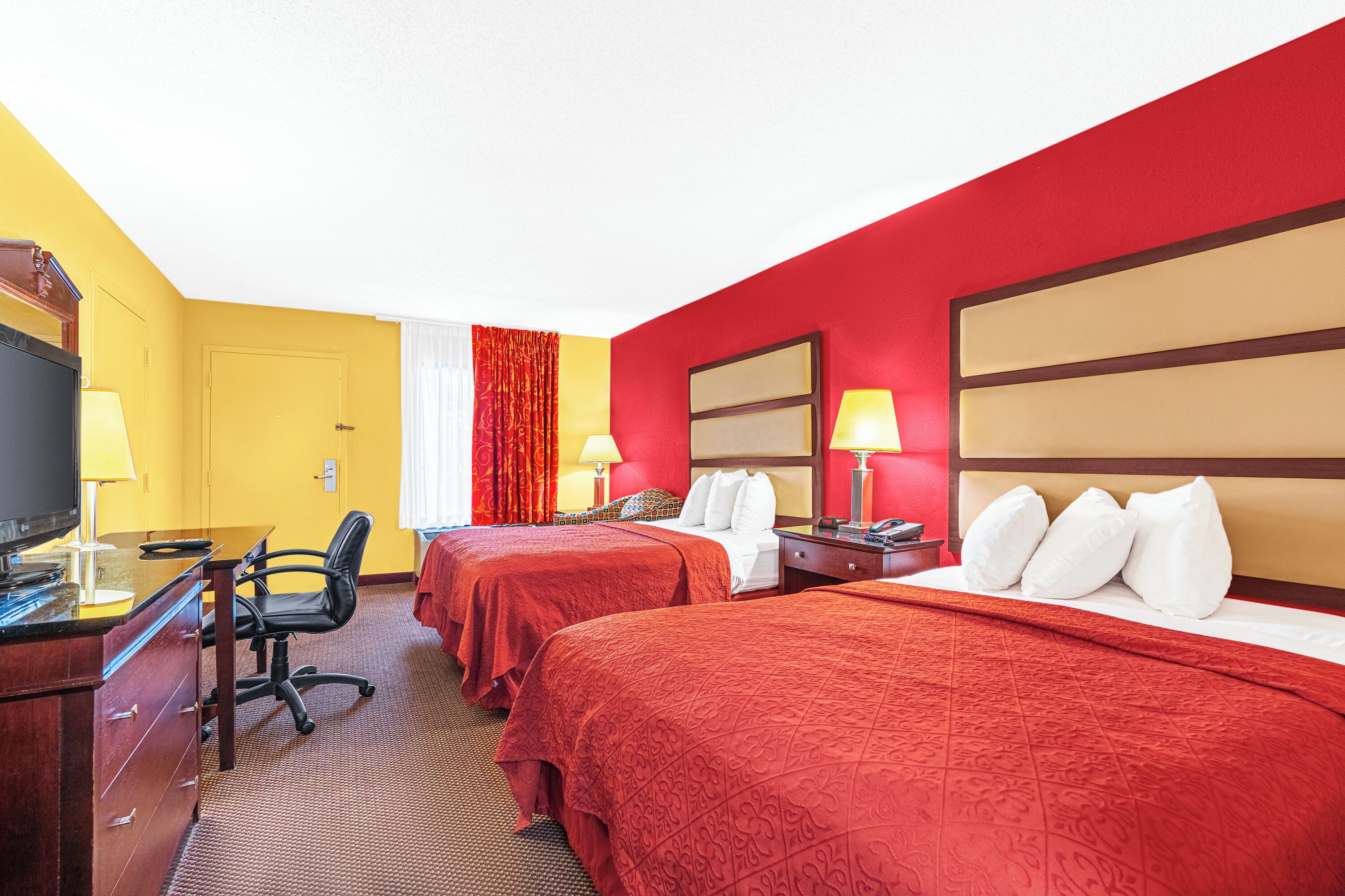 Ein Hotelzimmer mit zwei Betten, einem Schreibtisch, einem Computer, einem Stuhl und einem Fernseher.