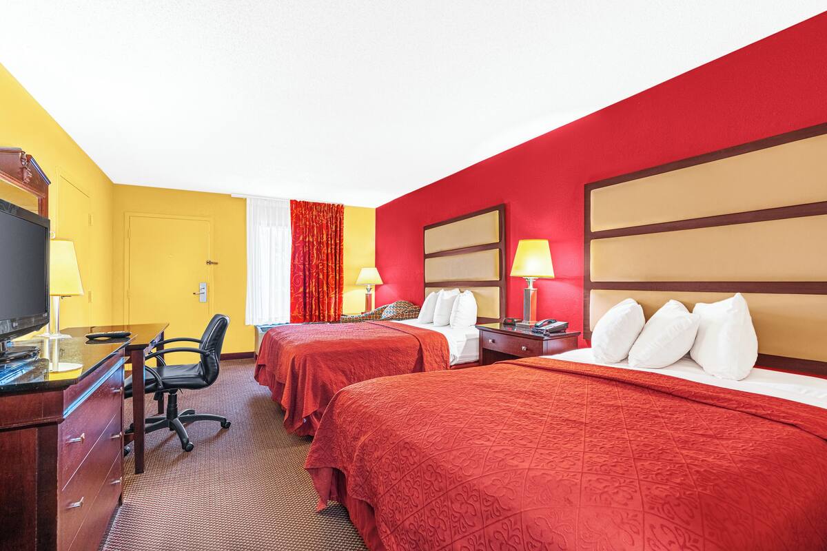 Quarto de hotel com duas camas, uma mesa de escritório com computador, uma cadeira e uma televisão.