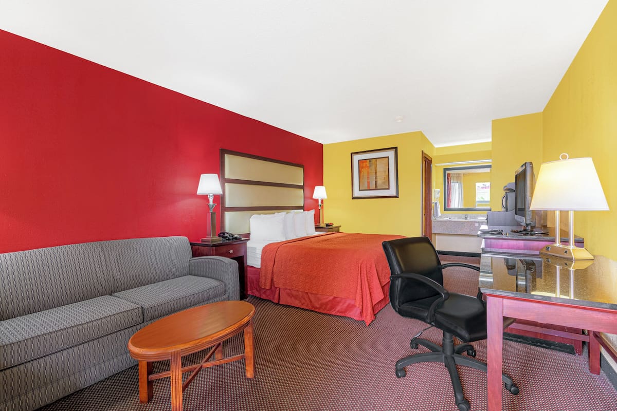 Quarto de hotel com esquema de cores vermelho e amarelo, uma cama, um sofá, uma escrivaninha e uma cadeira.