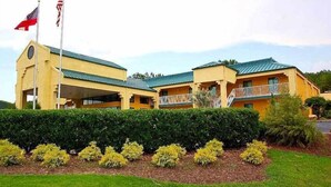 A yellow building with a green roof, two flagpoles with flags, and a well-maintained hedge. - Welcome Inn (Milledgeville)