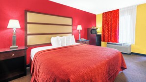 A hotel room with a red and yellow color scheme, a large bed with white bedding, two bedside tables with lamps, a TV, and a window with red curtains. - Welcome Inn (Milledgeville)